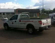 White pickup truck with a ladder rack, branded with Portes de Garage Citadelle parked in a commercial lot.
